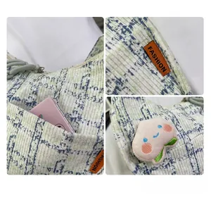 Detail of light green corduroy tote bag with blue patterns, fashion tag, and peach charm