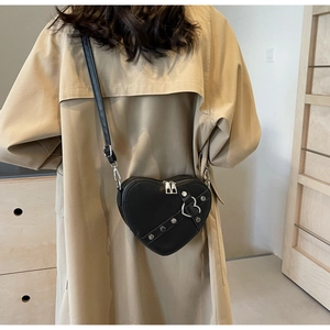 Vue détaillée du sac à bandoulière noir en forme de cœur avec clous sur un trench