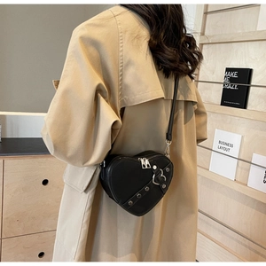 Détail d'un sac bandoulière noir en forme de cœur avec rivets porté sur un manteau beige