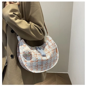 Detail of tweed hobo bag featuring peach plush charm and blue woven zipper puller