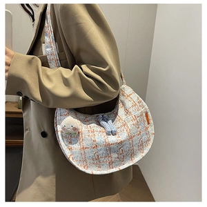 Macro view of blue tweed half-moon bag with woven zipper pull and peach plush pendant