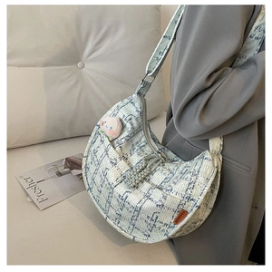 Detail of light blue jacquard half-moon bag featuring a peach pin and orange tag