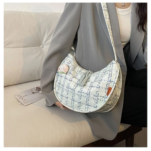 Detail of tweed crescent bag with blue check pattern and peach plush charm on a model