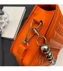 Gros plan d'un sac en cuir orange vif avec chaîne argentée et détails de quincaillerie