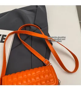 Détail de la bandoulière réglable en cuir et boucle argentée sur un sac orange matelassé