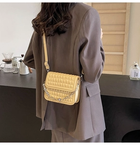 Détail d'un sac bandoulière jaune matelassé avec chaîne porté par un mannequin en café