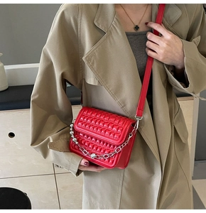 Détail du sac bandoulière rouge matelassé avec chaîne argentée porté sur un manteau