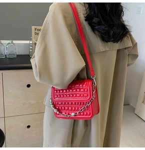 Détail du sac bandoulière matelassé rouge avec chaîne en argent porté par un mannequin