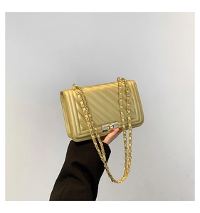Detail of gold quilted crossbody bag with metal chain strap and turn-lock closure