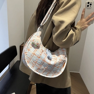 Houndstooth crossbody bag with peach plush charm shown on a female model
