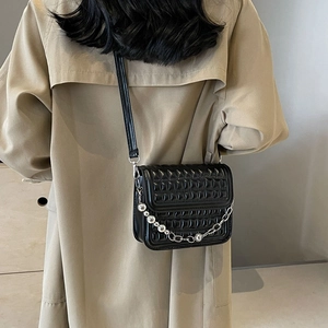 Sac bandoulière noir matelassé avec chaîne à boules d'argent porté sur un trench-coat