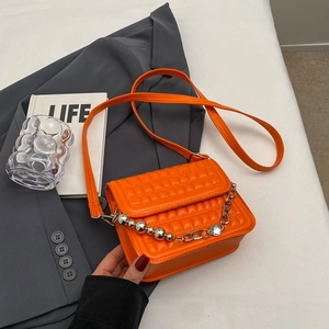 Petit sac carré matelassé orange avec poignée chaîne argentée sur veste grise