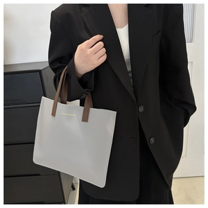 Detail of light gray faux leather tote bag with gold logo and brown shoulder straps