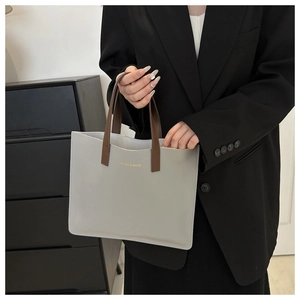 Detailed view of light gray leather tote bag with brown handles and golden text