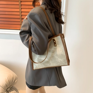 Vintage canvas tote bag with brown leather trim shown on shoulder in a minimalist setting