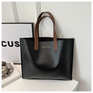 Detail view of black matte tote bag with contrast brown handles and gold logo text