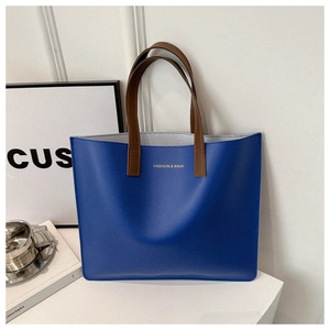 Close-up of blue tote bag with gold logo, brown handles, and clean stitching detail