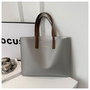 Detail of grey-blue leather tote bag with gold lettering and slim brown handles