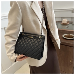 Close-up of black quilted leather shoulder bag with golden chain and logo on the model