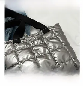 Close-up of metallic silver quilted tote bag with black strap and square stitching detail