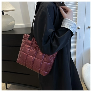 Detail of burgundy quilted tote bag with metallic finish and wide black strap
