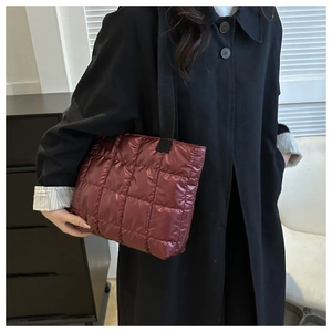 Deep red quilted tote bag with square stitching and wide black strap shown on a model