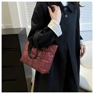 Detail of burgundy quilted tote bag with glossy finish and wide black shoulder strap