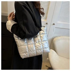 Silver quilted puffer handbag with black strap worn by a model in a modern interior setting