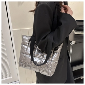 Detail of silver quilted puffer tote bag with metallic finish and black woven strap