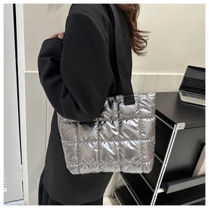 Detail of silver quilted puffer tote bag with metallic texture and black shoulder strap