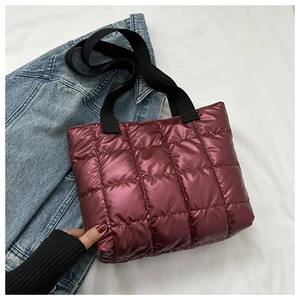 Detail of burgundy quilted puffer tote bag with glossy finish and black handles