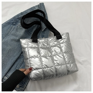 Close-up of quilted silver metallic tote bag with black woven handles and soft padded texture