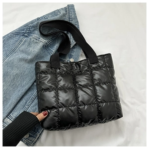 Detail of black quilted puffer handbag with woven handle on a white cloth surface