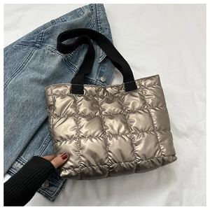 Detail of champagne gold quilted tote bag with metallic finish and wide black straps