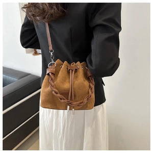 Gros plan d'un sac seau en daim marron avec poignée tressée et détails du cordon