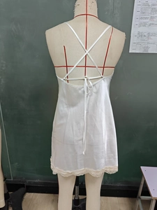 Detailed back view of white satin slip dress featuring crisscross straps and lace trim