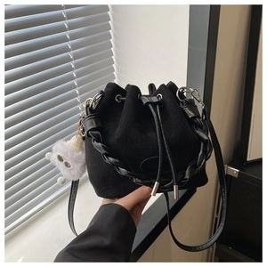 Détail du sac seau noir en daim avec poignée tressée et breloque pompon blanc sur un rebord