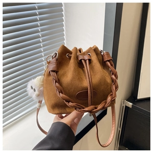 Détail du sac seau en daim caramel avec poignée tressée et breloque pompon blanc doux