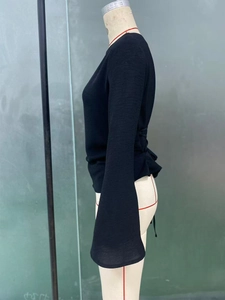 Detail of black knit top featuring dramatic bell sleeves and side lace-up styling