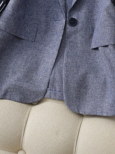 Detailed view of blue linen blazer fabric texture with black button and flap pocket detail