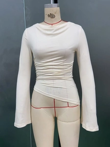 Detail of off-white long sleeve top featuring ruched waist and asymmetrical hemline