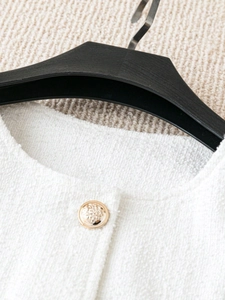 Detailed close-up of premium white tweed texture and embossed gold metal button on jacket