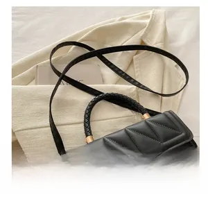 Detail of black quilted square bag with woven handle and gold hardware on beige blazer
