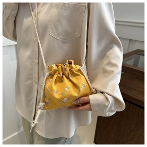 Close-up of yellow drawstring bucket bag featuring floral embroidery and cotton rope strap