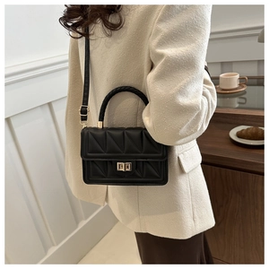Detail of black quilted crossbody bag with gold square lock and woven handle on model