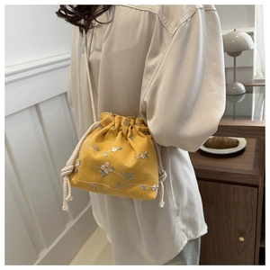 Detail of yellow canvas bucket bag with white floral embroidery and woven rope strap