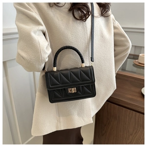 Detail of black quilted square bag with gold twist lock and woven handle on a model