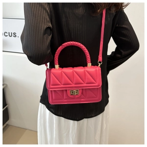 Detail of rose red quilted crossbody bag with gold square buckle and woven handle on model