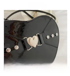Détail du sac coeur en cuir verni noir avec boucle dorée et rivets argentés