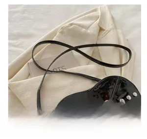 Détail du sac à bandoulière noir en forme de cœur avec boucles et rivets métalliques